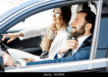 Elegante Geschäftsmann Anziehen der Riegel während der Fahrt ein Auto mit geschäftsfrau Stockfoto