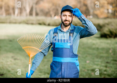 Porträt eines professionellen männlichen Kehrmaschine oder Gärtner in Uniform stehend mit Rechen im Garten Stockfoto