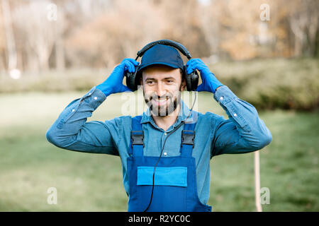 Professionelle Kehrmaschine oder Gärtner Kopfhörer tragen, das Hören von Musik während der Arbeit im Freien Stockfoto