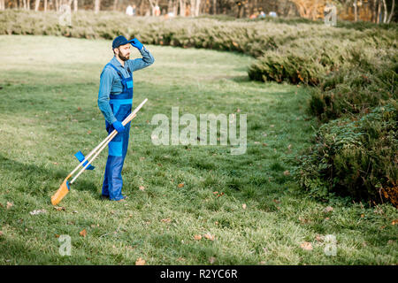 Professionelle Kehrmaschine oder Gärtner in Uniform zu Fuß mit der Reinigung der Werkzeuge im Garten Stockfoto