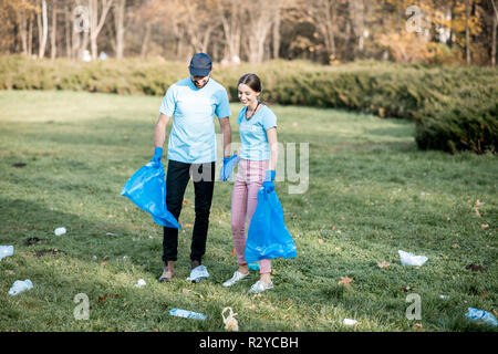 Mann und Frau Freiwillige in blauen T-Shirts gekleidet, Reinigung öffentlicher Garten aus plastik Müll in die Taschen Stockfoto