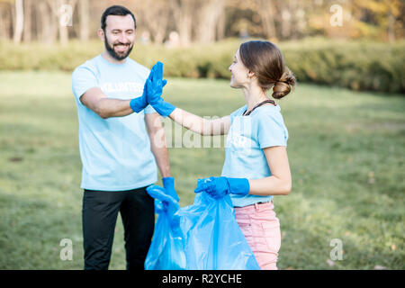 Portrait Of Happy Freiwillige in blauen T-shirts fünf mit Händen stehend mit Taschen voller Müll nach dem Park Reinigung Stockfoto