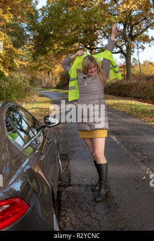 Frau Kraftfahrer durch ihr Auto Kämpfe auf eine reflektierende Sicherheitsweste zu setzen Stockfoto