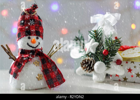 Schneemann mit Tannenbaum, Geschenkboxen und Weihnachtsbeleuchtung im Hintergrund. Mit Schnee Effekt Stockfoto