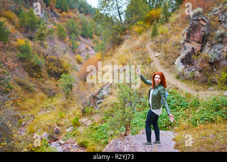 Tolle Frau mit einem Rucksack Touristen bewundert die Mountain Rock. Hübsche weibliche Wanderer unter selfie oder Live Video Stream vlog in Bergen Fores Stockfoto