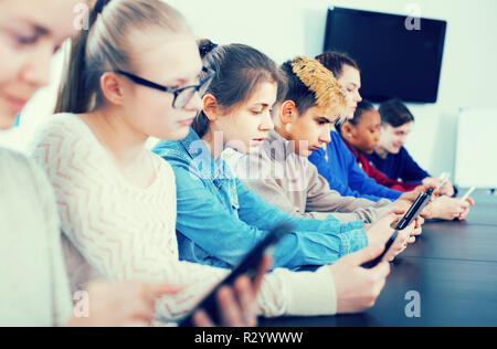 Positive europäische Mitschüler über ihre Smartphones intensiv während der Klassen Stockfoto