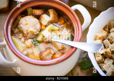Gemüsesuppe mit Bohnen und Hackfleischbällchen in eine keramische Schüssel auf eine weiße Holztisch Stockfoto