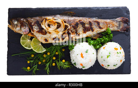 Blick von oben auf die ganze Forelle gebacken mit Reis, gegrillte Zwiebeln, grünen, Konserven Erbsen und Kalk auf Schwarz mit Board. Auf weissem Hintergrund Stockfoto