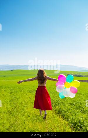 Happy girl In den Wiesen der Toskana mit bunten Luftballons, gegen den blauen Himmel und grüne Wiese. Toskana, Italien Stockfoto