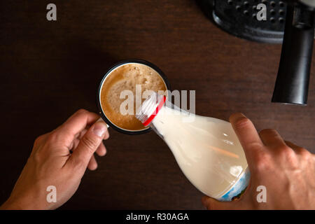 Foto der Kaffeemaschine, die Hände des Menschen gießen Milch in die kaffeetasse Stockfoto