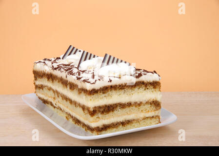 Tiramisu auf einer rechteckigen Platte auf Holz Tisch mit orangefarbenen Hintergrund. Tiramisu ist ein beliebtes italienisches Dessert mit Schichten von Biskuit in Zusammenarbeit getränkt Stockfoto