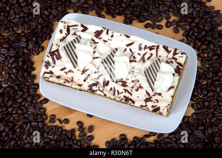 Tiramisu auf einer rechteckigen Platte auf Holz Tisch von frischen Kaffeebohnen umgeben. Tiramisu ist ein beliebtes italienisches Dessert mit Schichten von Schwamm c Stockfoto