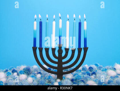 Ein 9-verzweigte Menorah (auch als Chanukiah oder Hanukiah) brennende Kerzen Hanukkah gegen einen hellblauen Hintergrund mit Licht und dar zu feiern. Stockfoto