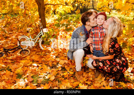 Foto des Küssens Eltern und Kinder im Herbst Park sitzen am Nachmittag Stockfoto