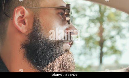 Eine brutale bärtigen Mann in Sonnenbrille ist ein Auto fahren. Stockfoto