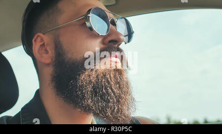 Eine brutale bärtigen Mann in Sonnenbrille ist ein Auto fahren. Stockfoto