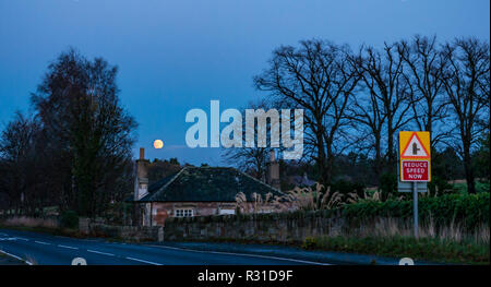 East Lothian, Schottland, Vereinigtes Königreich, 21. November 2018. UK Wetter: Ein helles Orange waxing gibbous Mond am Himmel in der Dämmerung über ein strassenrand Cottage niedrig wird angezeigt Stockfoto