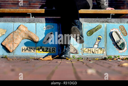 Hannover, Deutschland. 18 Nov, 2018. Eine junge Frau sitzt auf einer Bank mit relief Kacheln und modelliert Damenschuhe. Die Bank und andere Kunstwerke auf Figurinenplatz auf Schulenburger Landstraße wurden im Jahr 2010 von den Bewohnern der Hainholz Bezirk erstellt unter der Leitung von Künstler Siegfried Neuenhausen. Credit: Hauke-Christian Dittrich/dpa/Alamy leben Nachrichten Stockfoto