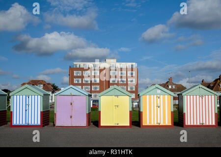 Brighton Seafront 5 Badekabinen, mit bunten Türen von Gelb, Pink, Schwarz Streifen hinter ist ein Appartement Gebäude und blauer Himmel Stockfoto