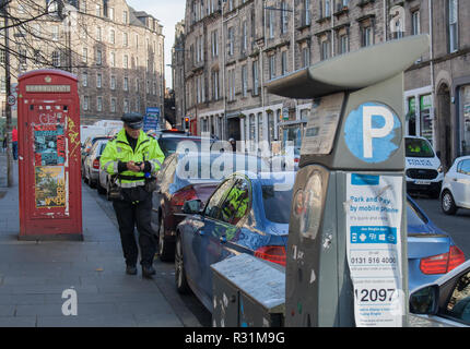 Parkwächter tragen einheitliche und Kontrolle der Autos auf einer Straße von Edinburgh, mit Parkuhr in den Vordergrund und rote Telefonzelle im Hintergrund Stockfoto