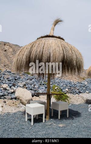 Hut, Schirm aus Stroh und Stühle auf dem schwarzen Sand vulkanischen Strand auf Teneriffa, Kanarische Inseln, Spanien Stockfoto