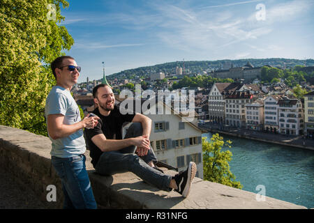 Aufgeregt hübscher junger Männer in Freizeitkleidung sitzt am Bahndamm im City Park. Fröhlich verträumtes sorglos Kerle Naturbetrachtung und die Stadt um. Lifestyle Konzept Stockfoto