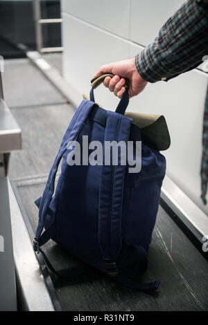 Des Menschen Hand mit einem Rucksack auf Gepäck Förderbandanlage am Check-in-Schalter am Flughafen. Blau Rucksack am Check-in-Schalter am Flughafen, Messen des Gewichtes. Der Flughafen Mitarbeiter registriert das Gepäck. Stockfoto