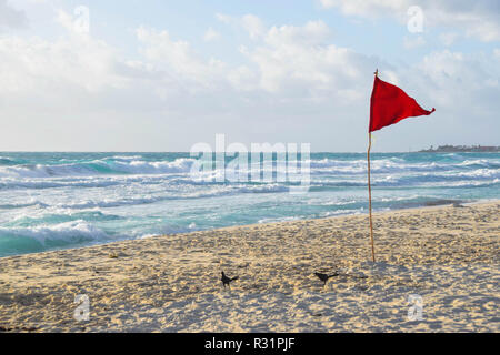 Blaues Wasser Wellen am Strand in Cancun, Mexiko, mit einer roten Fahne brechen Stockfoto