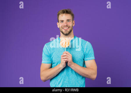 Mann essen großen bunten süßen Lutscher. Mann mit Borsten mag Lollipop. Cheat meal Konzept. Zucker schädlich für die Gesundheit. Kerl halten Lollipop candy violett unterlegt. Geschmack der Kindheit. Lollipop Spaß. Stockfoto