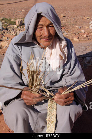 Marrakesch, Marokko - 21,02,2012: Eine freundliche alte typisch gekleidet Berber mann Handwerk Gurte von Stroh in den Ausläufern des Hohen Atlas. Stockfoto