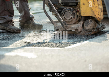 Arbeitnehmer mit Verdichter zu beenden patching Stoß in der Straße mit frischem Asphalt. Stockfoto