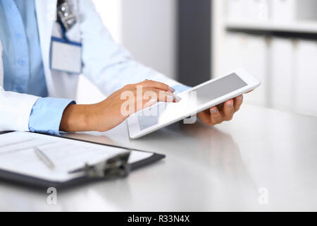 Unbekannte Arzt Frau mit Tablet Computer, während gerade in der Nähe von Fenster im Krankenhaus, in der Nähe der Hände. Medizin und Gesundheit Konzept Stockfoto