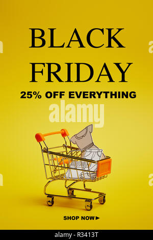 In der Nähe der kleinen Einkaufswagen mit Papier Kleidung auf gelbem Hintergrund, schwarzer Freitag Inschrift Stockfoto