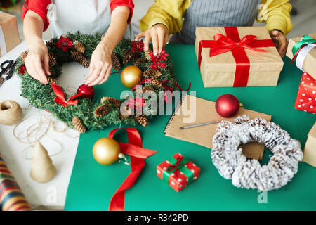 Die Hände der jungen Frau Schlichten mit Nadelholz Weihnachten Kranz, während Kollege helfen Ihr Stockfoto