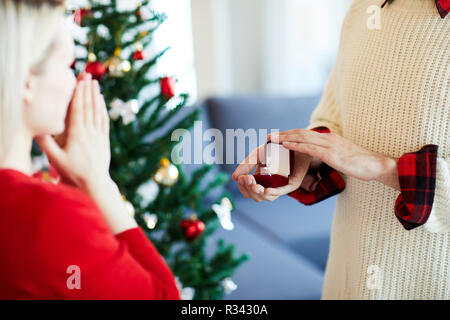Junger Mann Eröffnung kleine samt Box mit Verlobungsring während Vorschlag zu seiner Freundin am Heiligabend Stockfoto