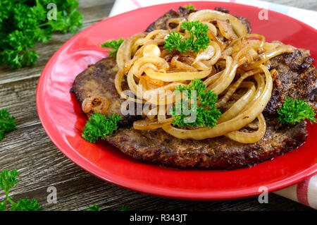 Saftige Scheiben gebratene Leber und Zwiebeln auf einem roten Schild. Stockfoto