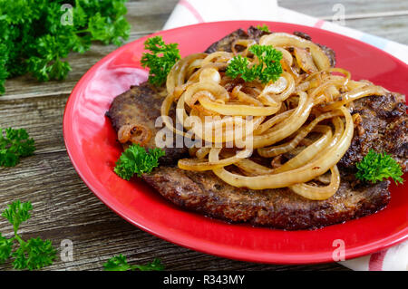 Saftige Scheiben gebratene Leber und Zwiebeln auf einem roten Schild. Stockfoto