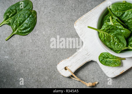 Blick von oben auf die grüne saftige Spinatblätter in der Schüssel auf weißem Holz Schneidebrett Stockfoto