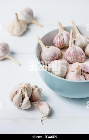 Blau Keramik Schüssel mit Knoblauch, Zwiebeln und mehrere geschälte Knoblauchzehen auf weissem Holztisch Stockfoto