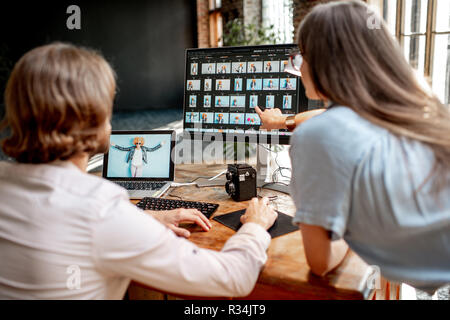 Junges Paar von Fotografen arbeiten mit Porträts der Frau am Arbeitsplatz mit zwei Computern im Studio Stockfoto