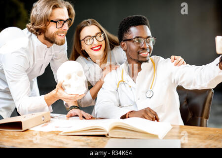 Gruppe von einem Jungen multi Ethnizität Ärzte oder Medizinstudenten in Uniform, selfie Foto, während drinnen Studieren Stockfoto
