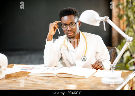 Porträt einer jungen afrikanischen Ethnie Arzt oder Medizinstudent in Uniform während der Arbeiten oder Studieren, im Büro oder im Unterrichtsraum Stockfoto