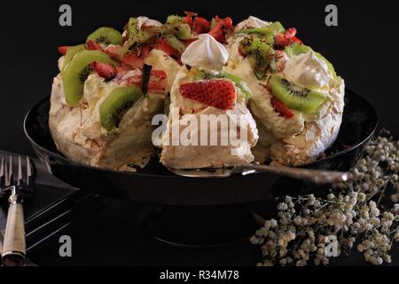 Pavlova.. Golden äußere Kruste mit einem herrlichen weichen Marshmallow center. Diese Aufnahme mit Besteck, Geschirr und getrocknete Blumen als Requisiten eingesetzt. Stockfoto