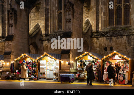 Gotische Kathedrale von Winchester bei Nacht und Weihnachtsmarkt in der mittelalterlichen Stadt Winchester mit Weihnachtseinkäufern, die durch hölzerne Chalets bummeln. England Stockfoto