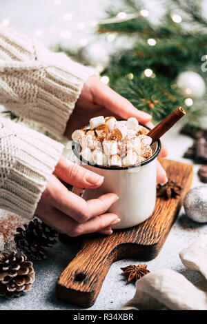 Weihnachten trinken heiße Schokolade mit Marshmallows. Weibliche Hände halten gemütliche Tasse heiße Schokolade mit Marshmallows und Zimt über Weihnachten Baum bac Stockfoto