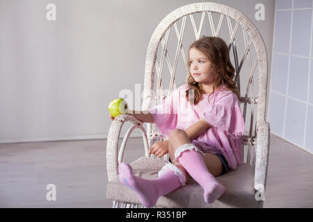 Das kleine Mädchen sitzt auf einem Stuhl und Grüner Apfel Stockfoto