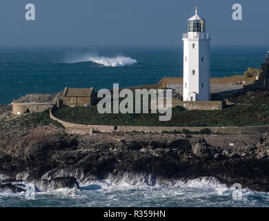 Nahaufnahme von Godrevy Leuchtturm, Teil der Insel und der kleine alte Wohnungen an der Seite. Brechende Welle im Meer hinter sich. Stockfoto