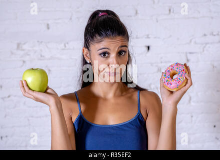 Schöne junge Frau versucht, die Wahl zwischen Apple und Krapfen in Gesund ungesunde Nahrung, Detox essen, Kalorien und Diät Konzept zu machen. Stockfoto