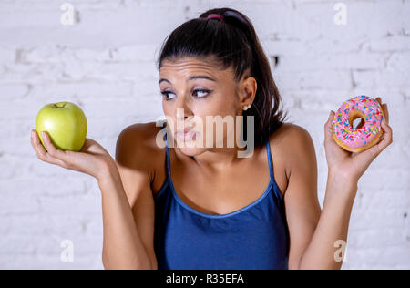 Schöne junge Frau versucht, die Wahl zwischen Apple und Krapfen in Gesund ungesunde Nahrung, Detox essen, Kalorien und Diät Konzept zu machen. Stockfoto