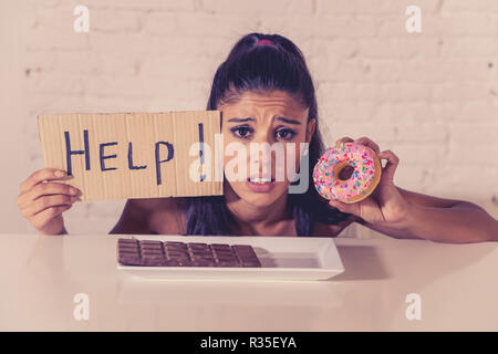 Junge besorgt Latin Frau Gefühl versucht und schuldig, Schokolade und Donuts um Hilfe zu bitten, in der Diät Kalorien Zucker Ernährung Essen ein Stockfoto